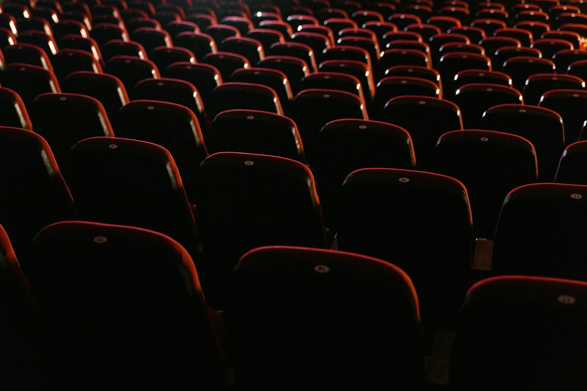 Rows of empty red theater seats in a darkened cinema auditorium