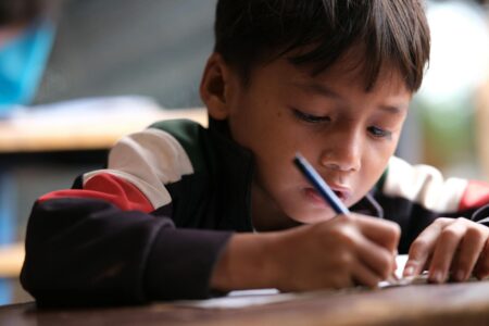 Child sitting at desk with pen and paper, writing