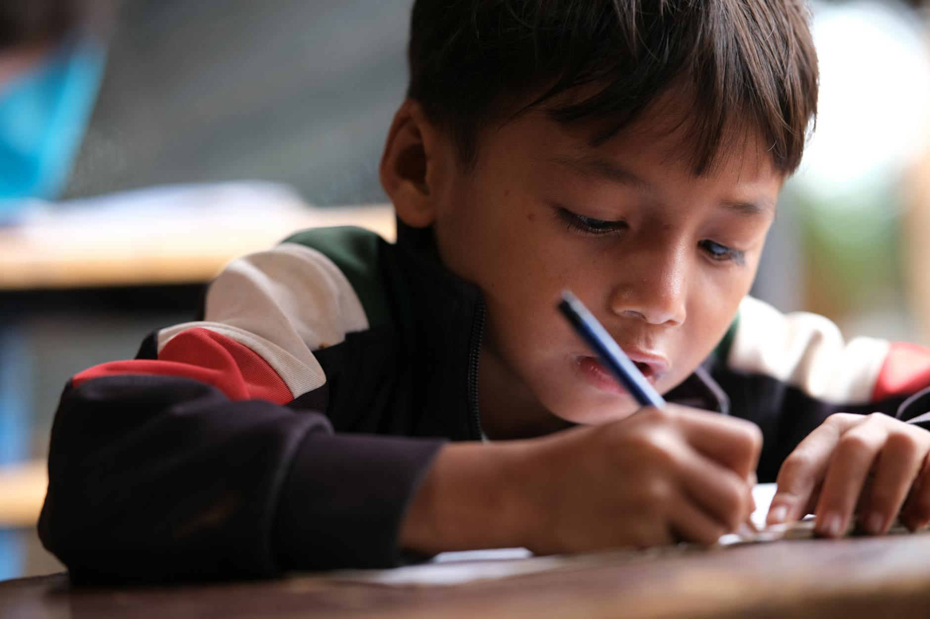 Child sitting at desk with pen and paper, writing