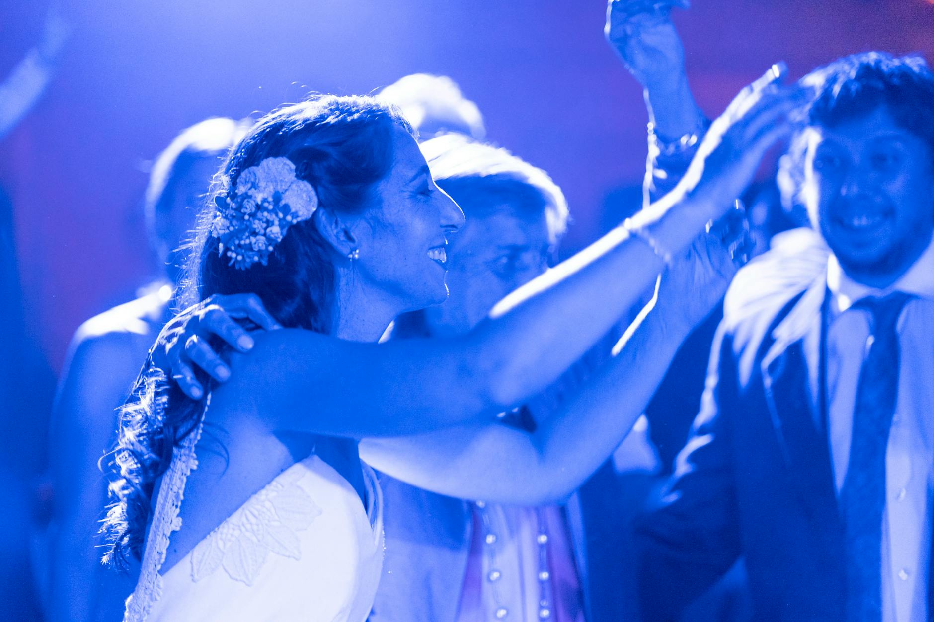 Wedding guests dancing enthusiastically at reception with DJ equipment and lighting in background