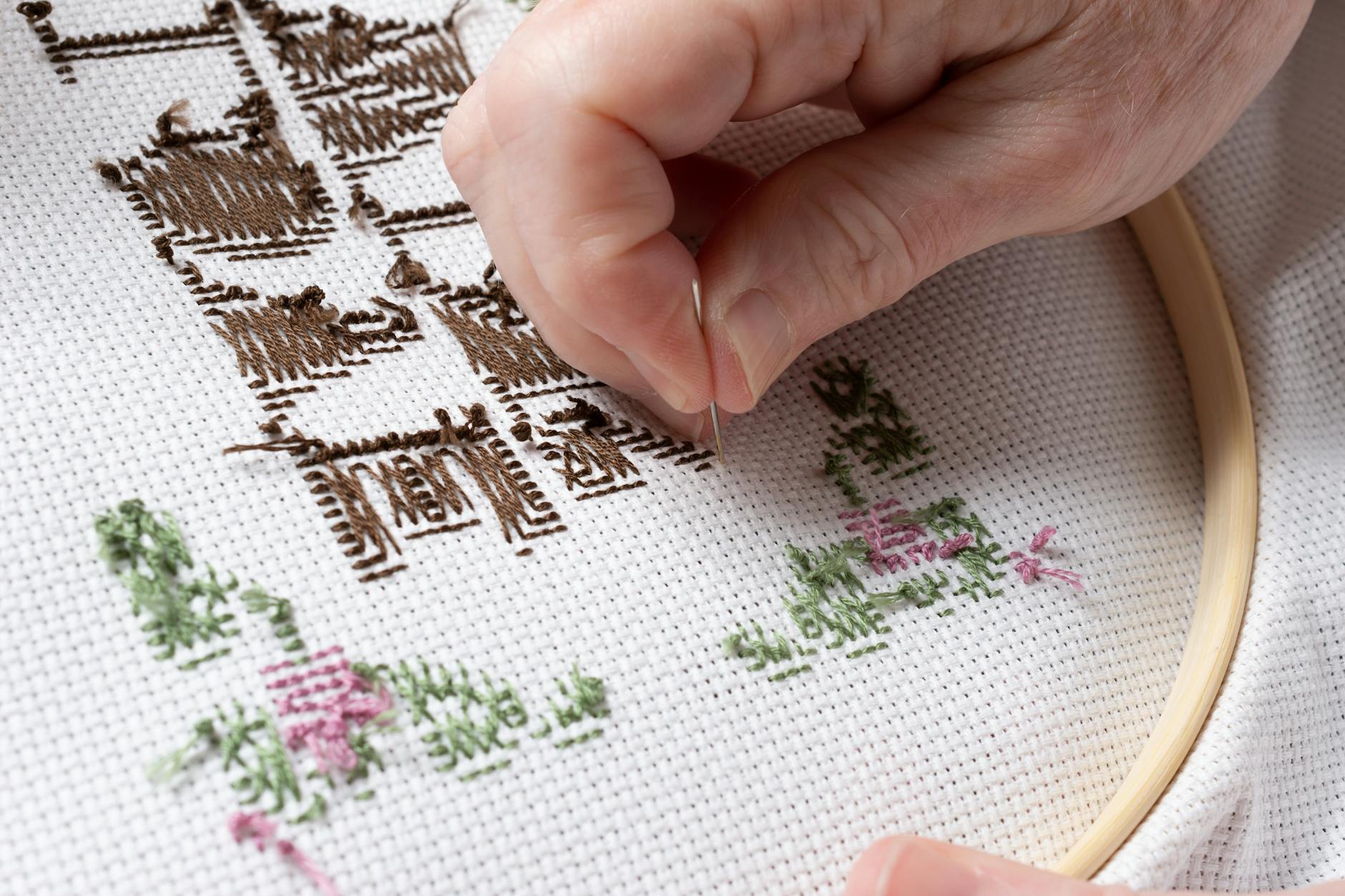 Close-up of hands doing decorative embroidery stitching on fabric with colorful thread