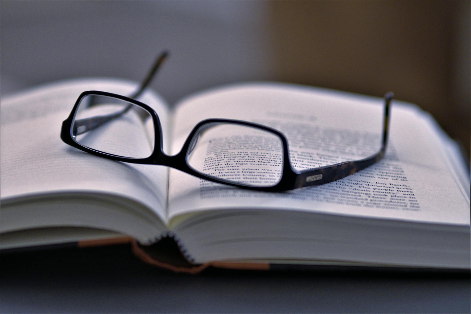 Reading glasses resting on an open book with text visible on pages