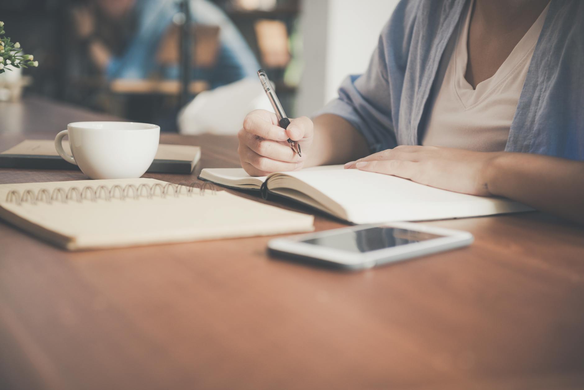 Woman writing intentions in a journal beside a coffee cup