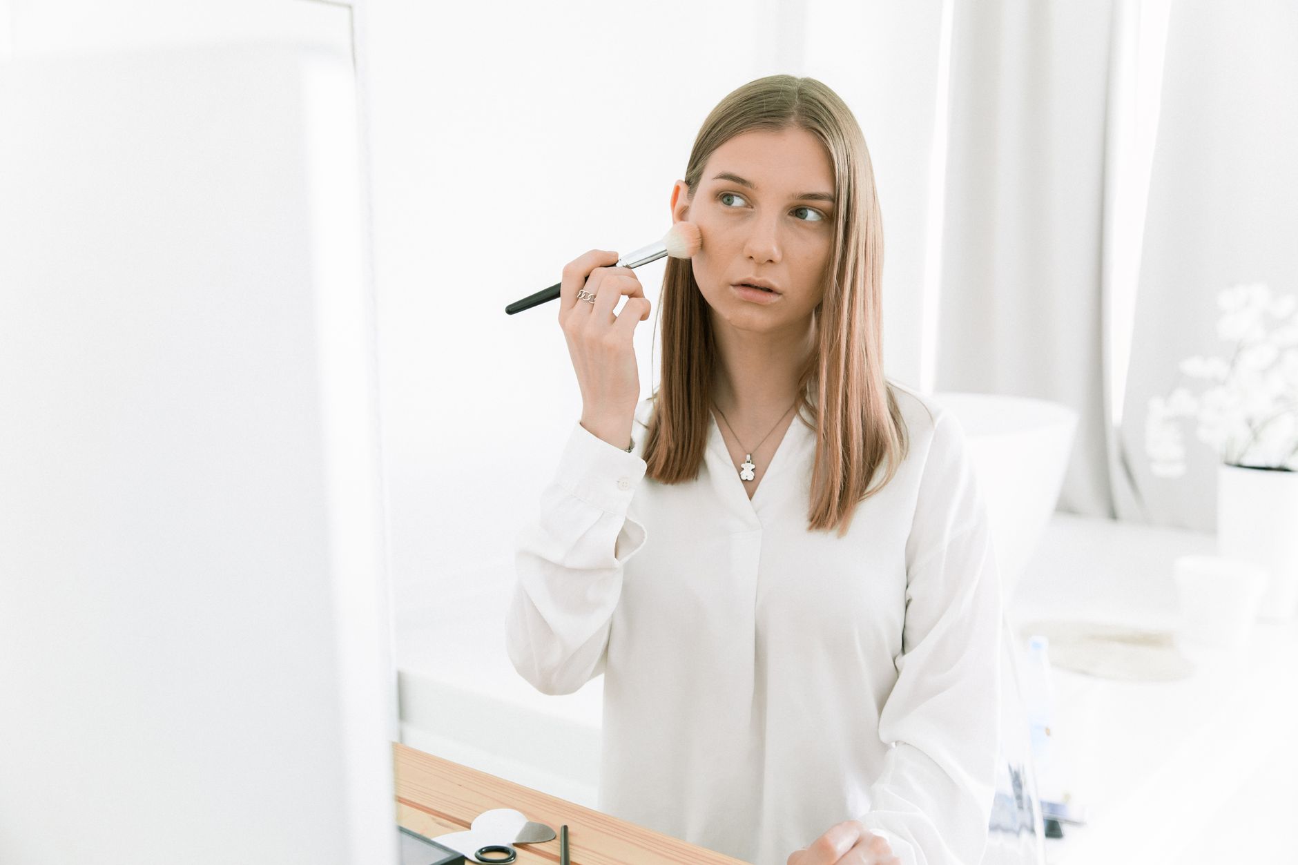 Woman blending blush onto cheekbones with fingers in natural light