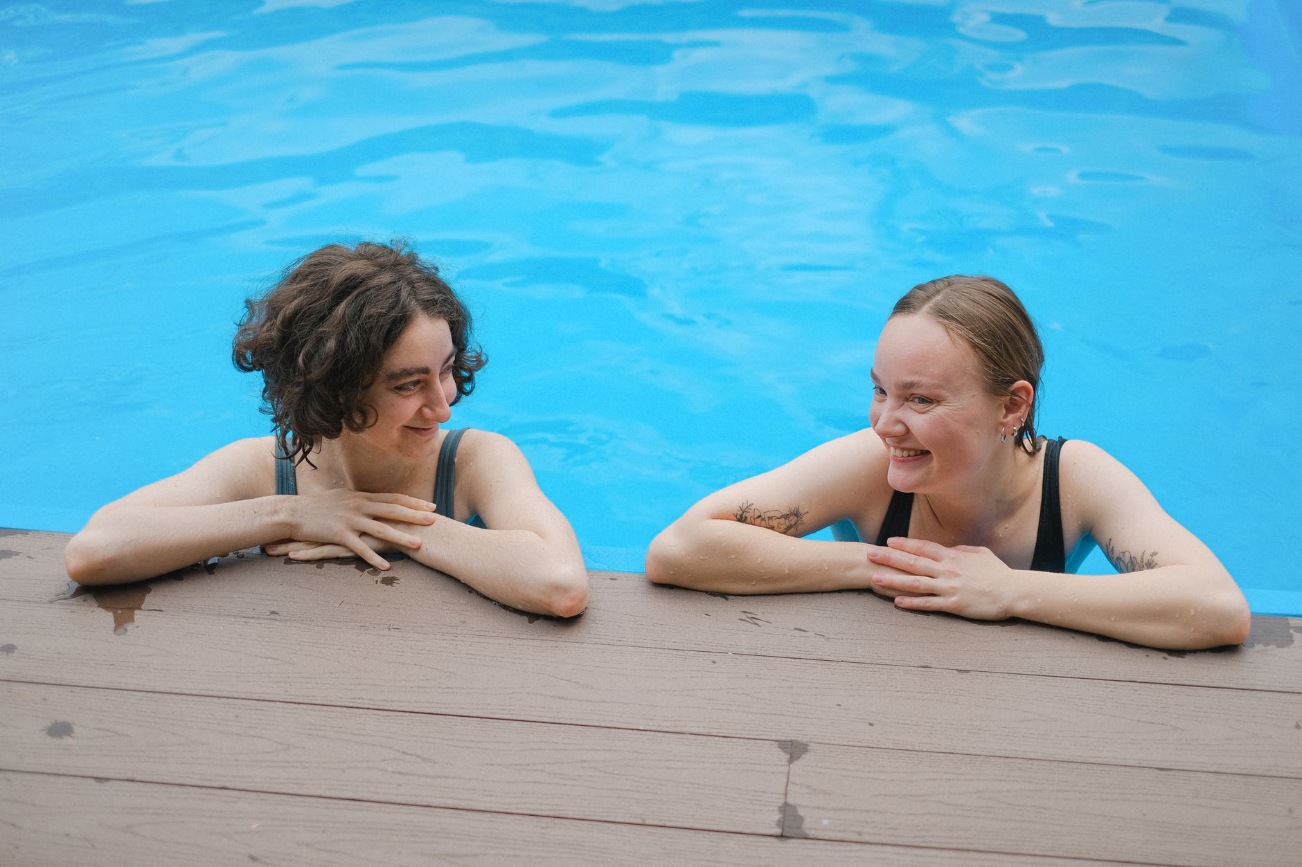 Two women in conversation near a pool, serious expressions