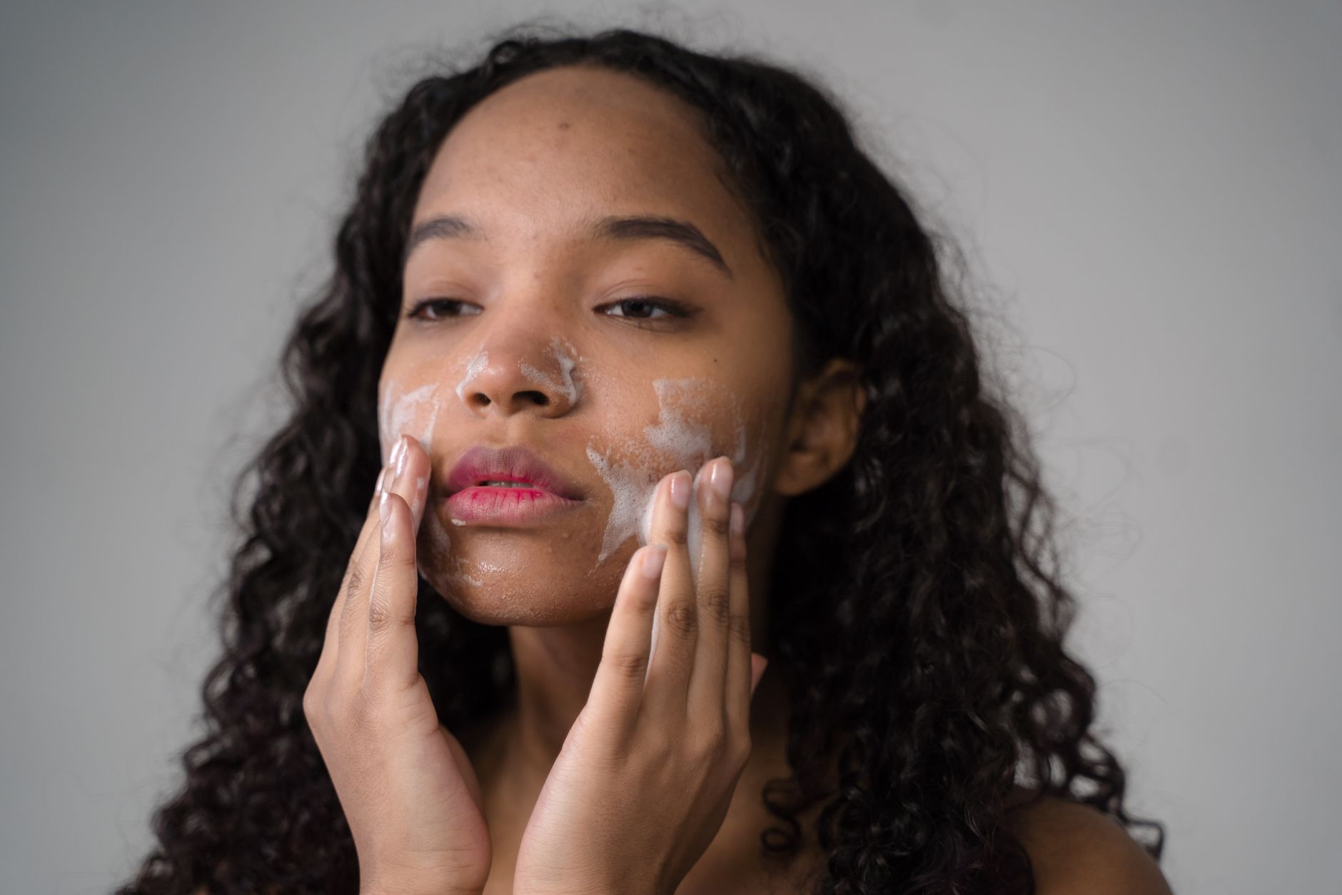 Woman gently applying a balm cleanser to her face in soft bathroom lighting