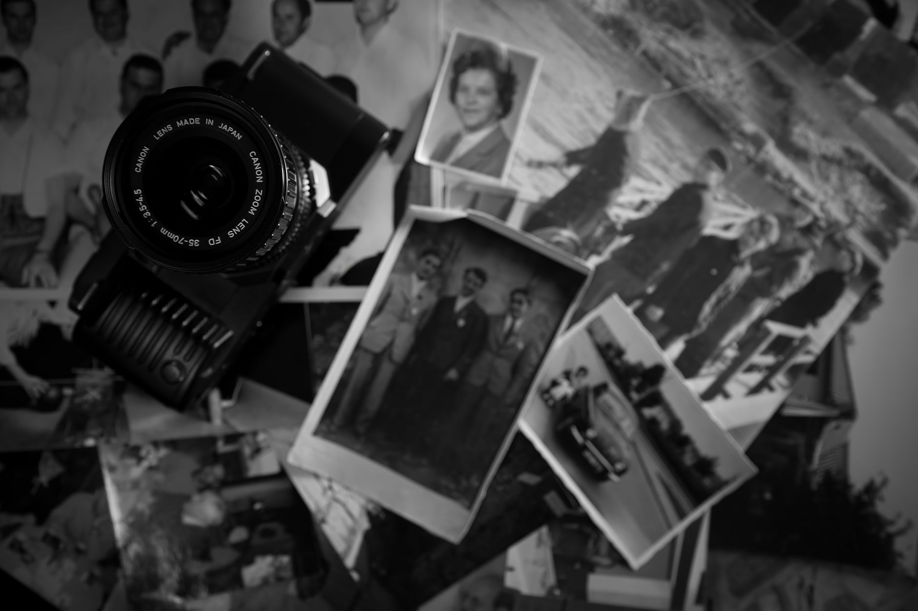 A collection of faded old photographs spread across a wooden table, evoking memory and the past
