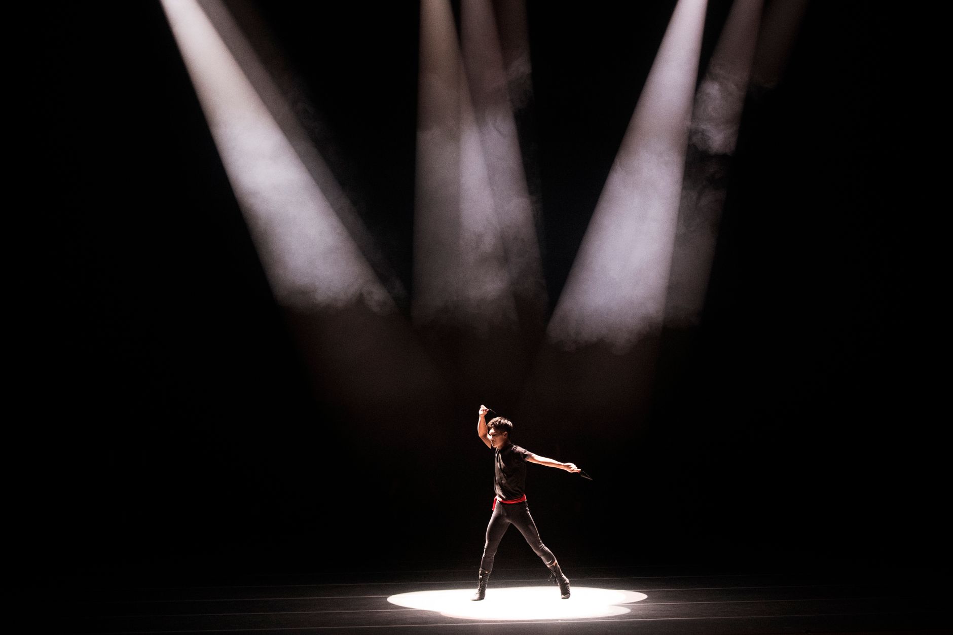 A person standing alone in a bright spotlight on a darkened stage