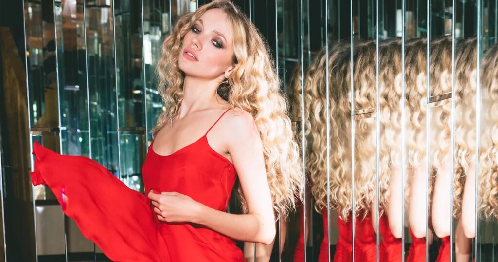 Red Is the Wedding Guest Color That Needs No Apology Woman in a red midi dress standing outdoors in natural light