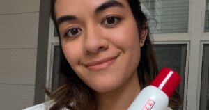 One/Size’s “Liquid” Blotting Paper Spray Actually Works — & Seeing Is Believing Woman checking her makeup in a mirror on a warm day