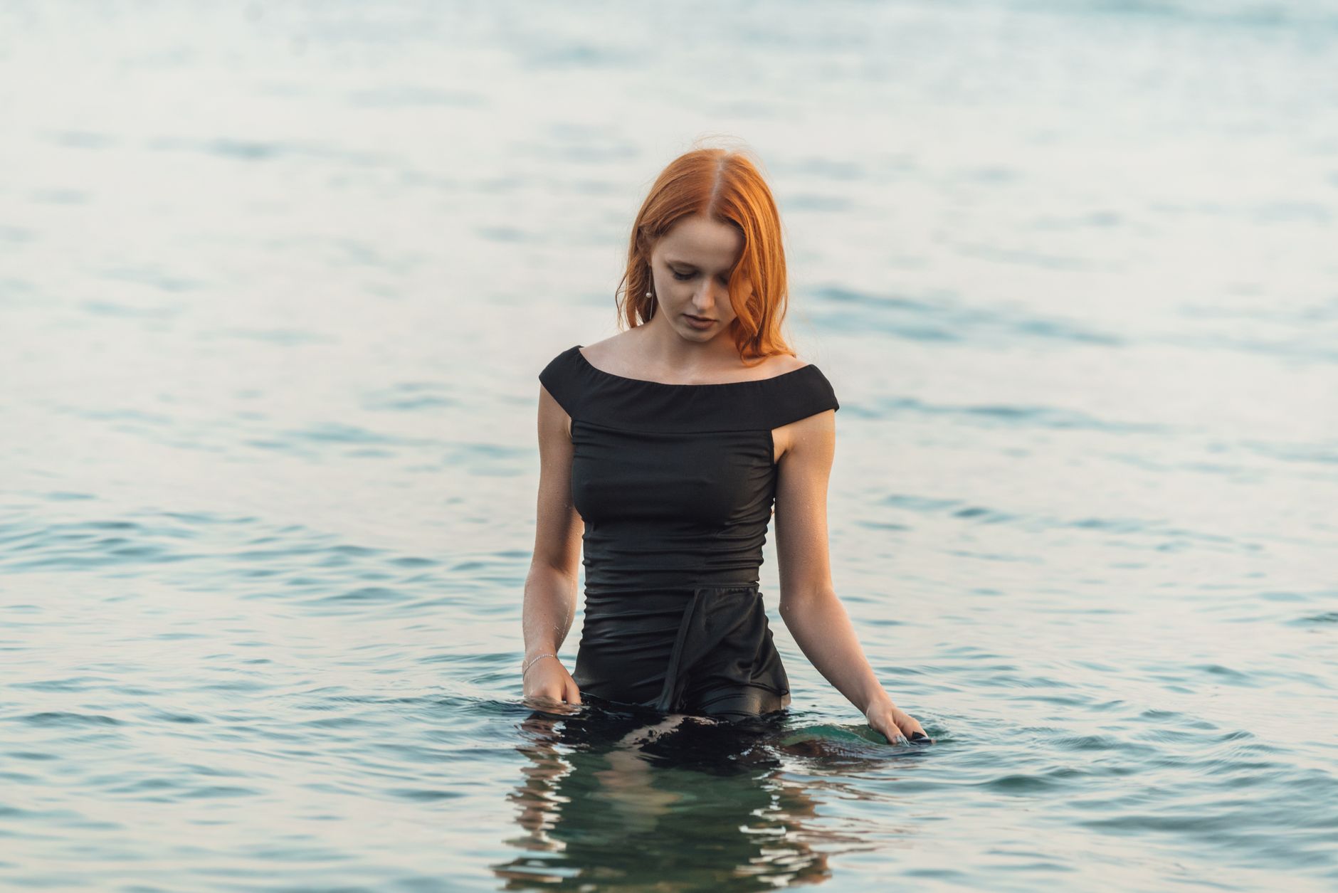 Woman standing near ocean waves at dusk, looking toward the horizon