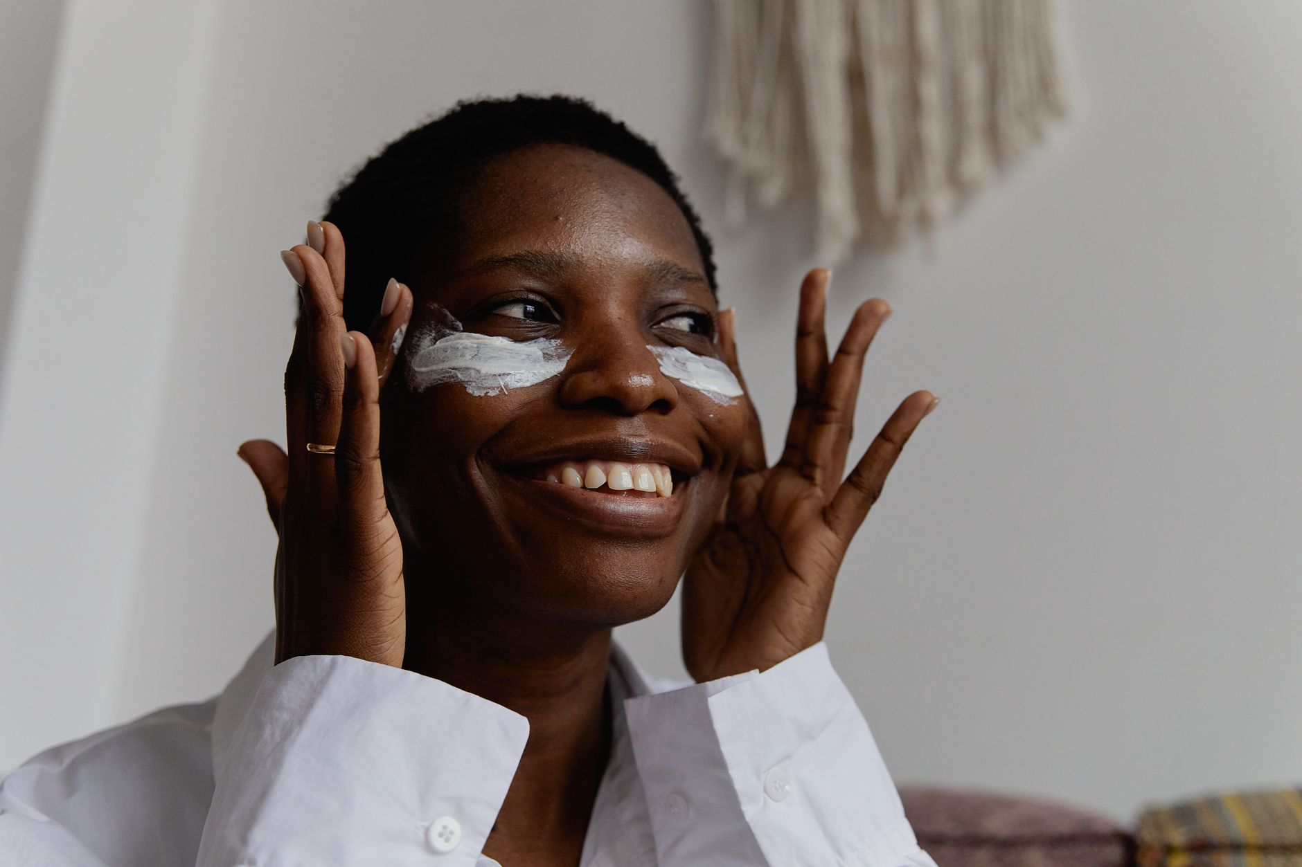 Black woman applying skincare product while looking in mirror