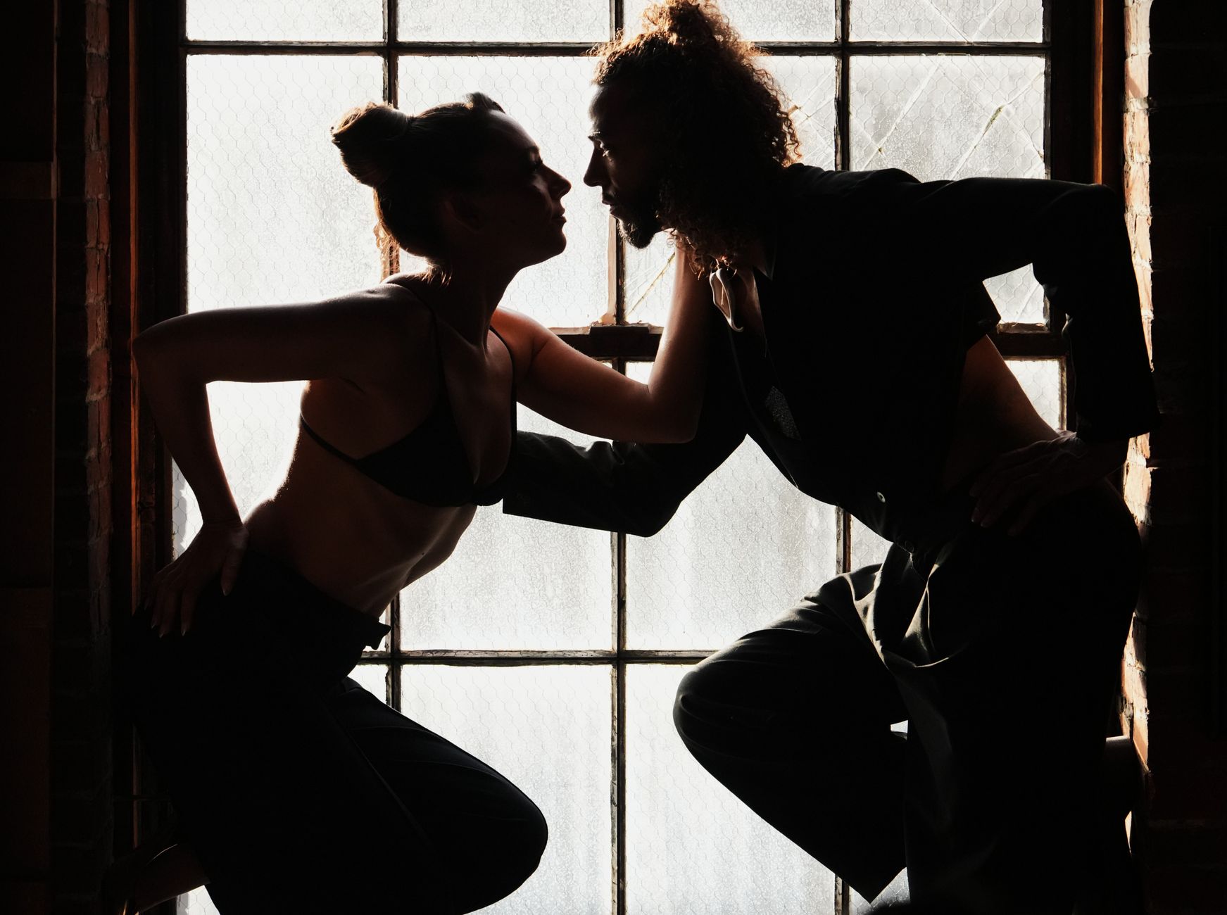 Silhouette of two people facing each other near a softly lit window