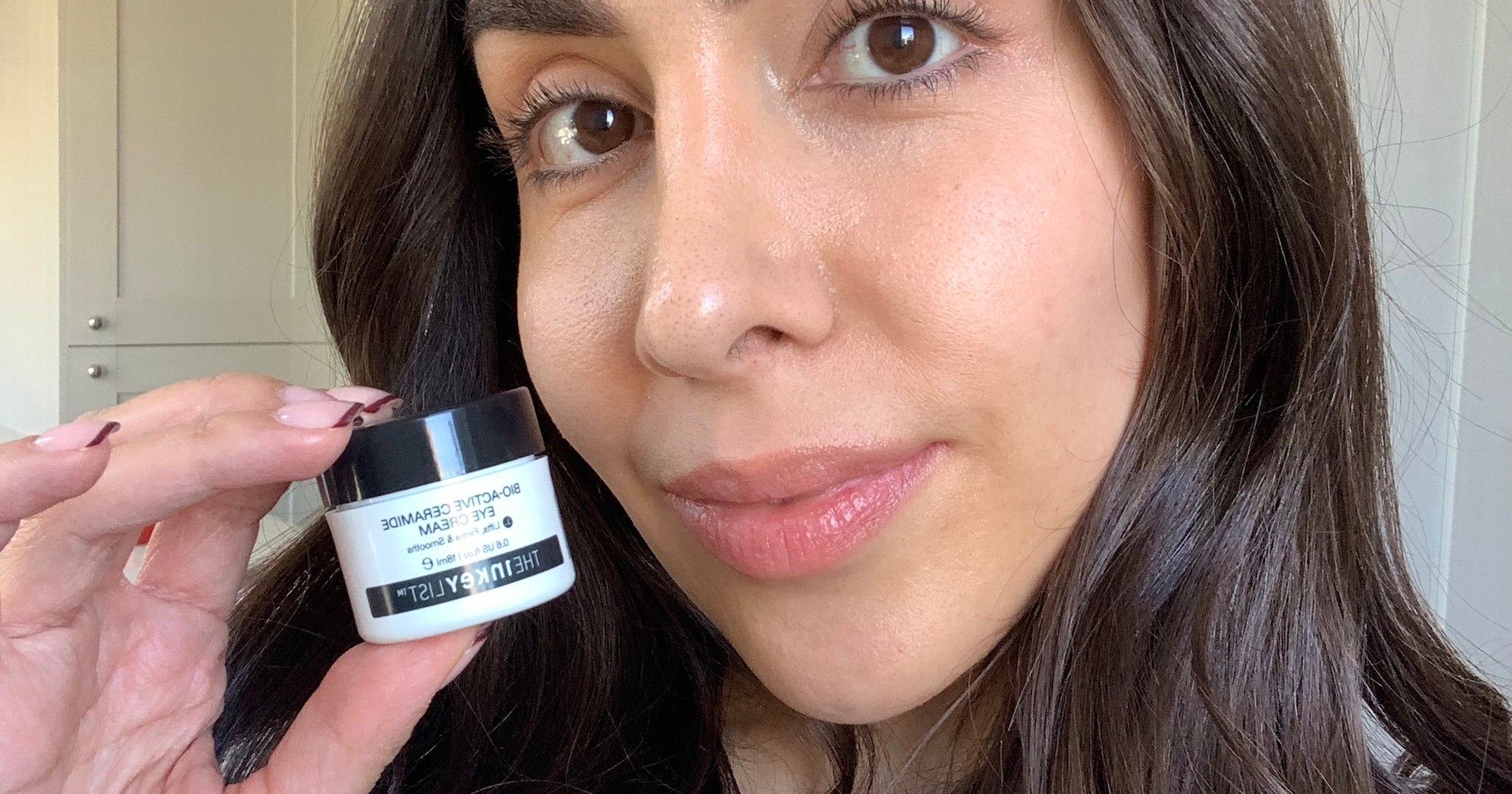 Woman applying eye cream in front of a bathroom mirror during a morning skincare routine