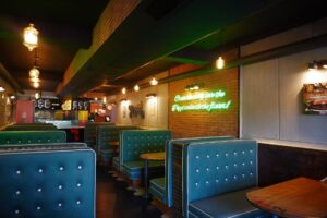Amelia Dimoldenberg Is Ending Chicken Shop Date at Its Peak Empty fast food restaurant booth with overhead lighting, evoking the casual intimacy of a low-key interview setting