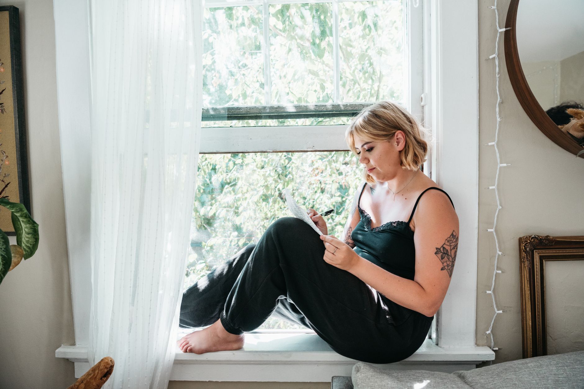 Woman writing in a journal at a window with soft natural light and fall foliage visible outside