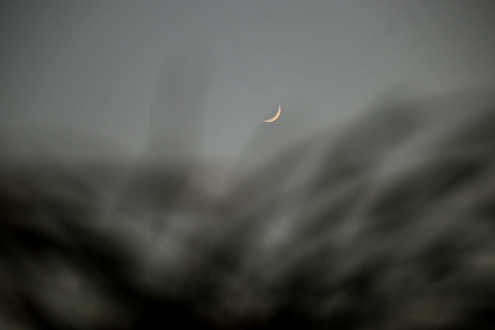 Crescent moon visible through a dark window at night