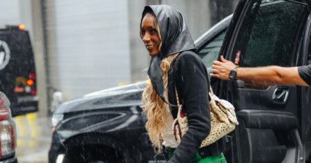 A fashion week attendee walking in the rain on a New York City street carrying an umbrella