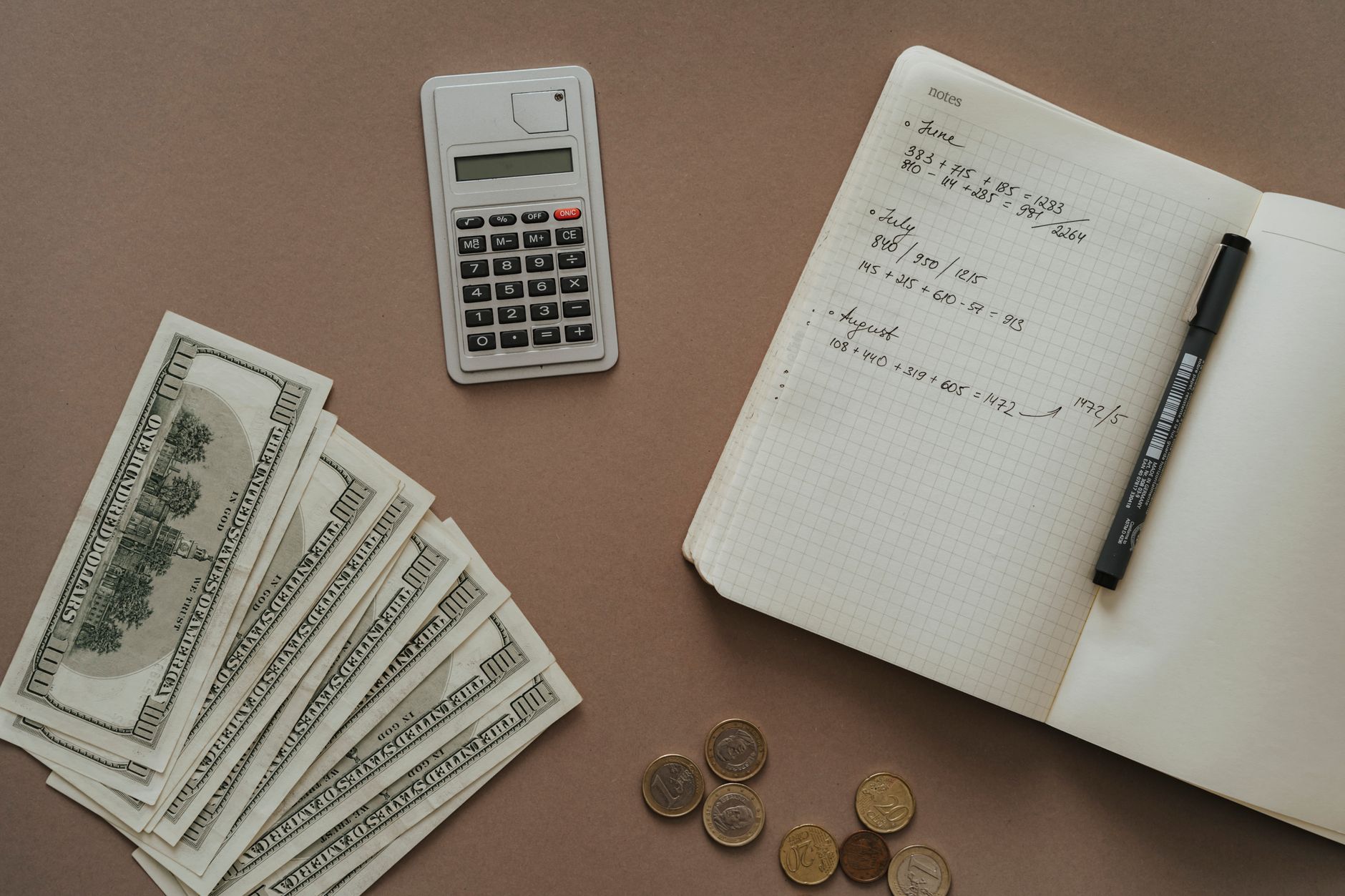 A person reviewing financial documents with a pen and notebook beside a laptop