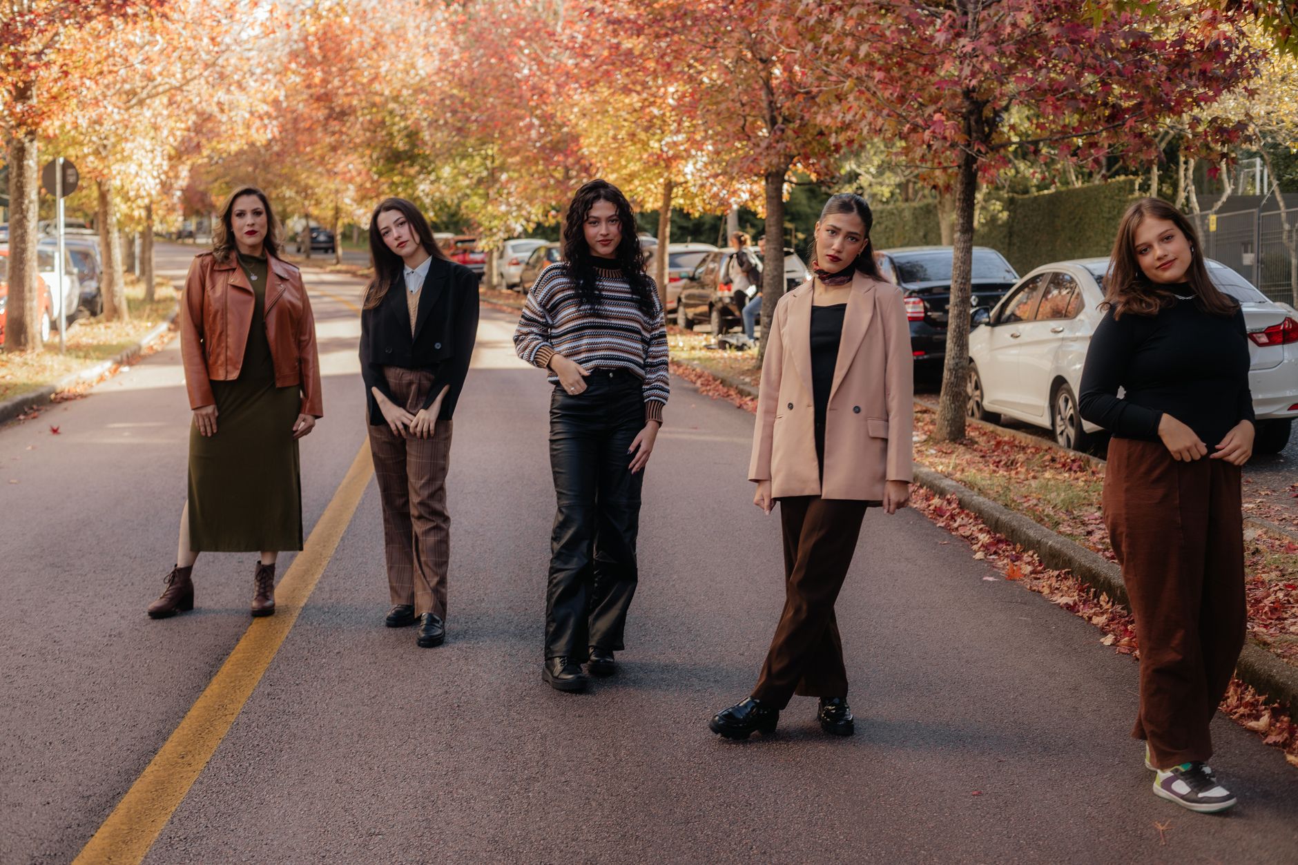 Woman in casual fall outfit wearing brown boots on a city sidewalk surrounded by autumn foliage
