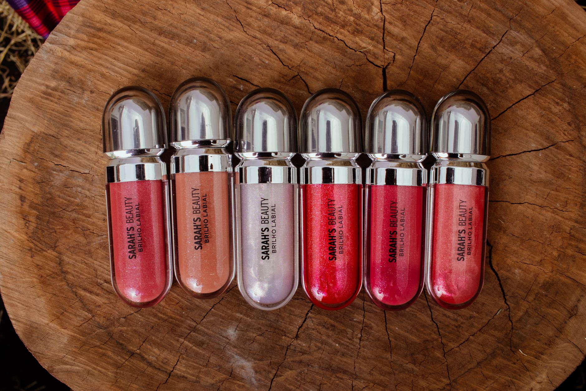 Close-up of lip gloss tubes and makeup products on a reflective surface