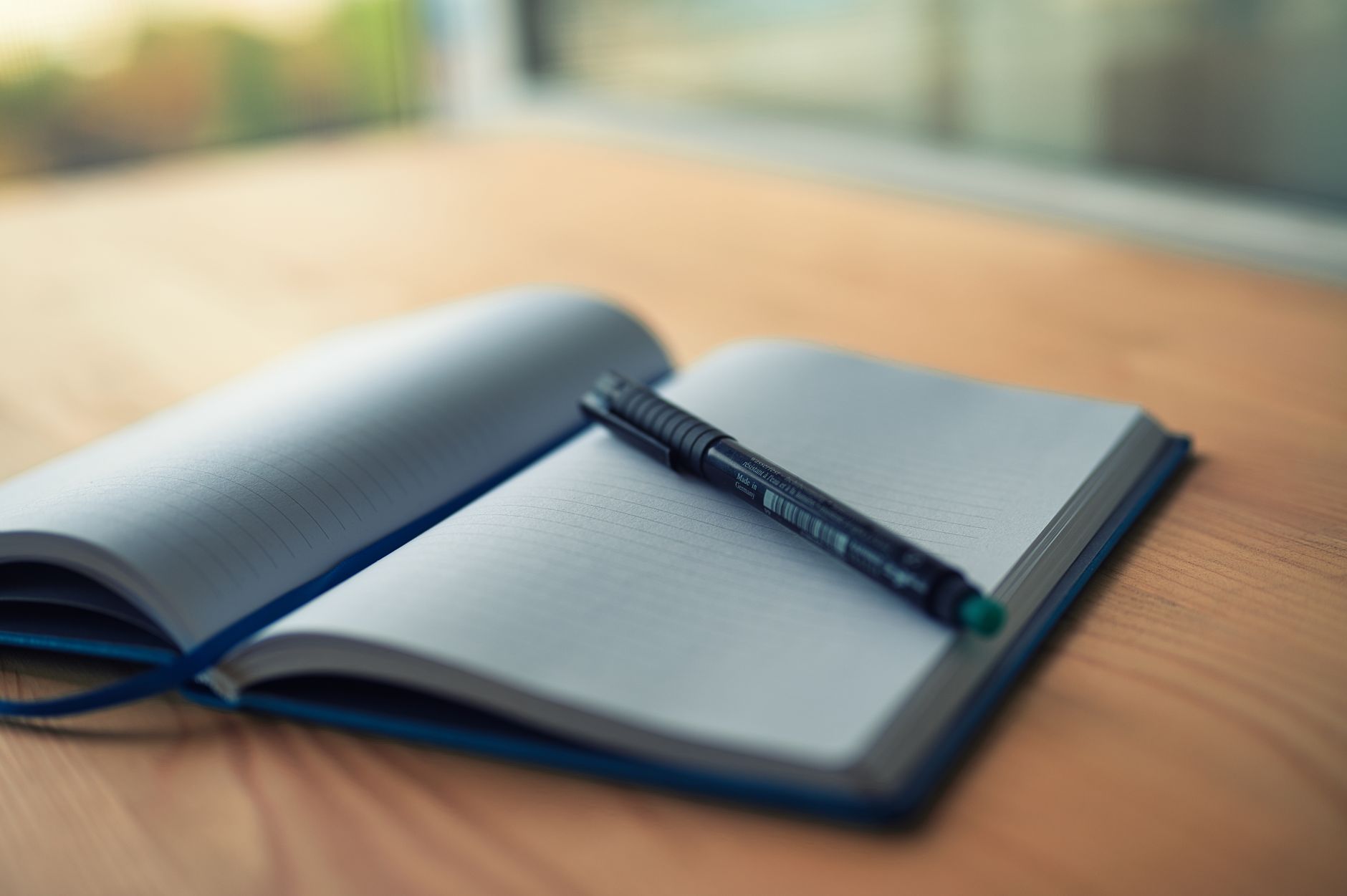 A person writing in an open journal on a wooden desk