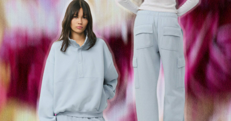The Matching Set Has Replaced the Outfit. Good. Woman wearing a matching grey lounge set sitting on a couch with a warm drink